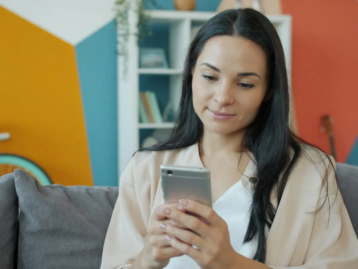 A woman on a sofa browsing a property app on her smartphone